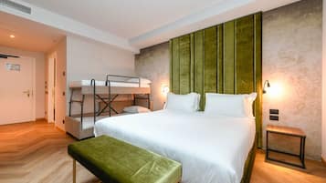 Una camera d'albergo con un letto a castello, un letto singolo, una panca verde e un tavolino.