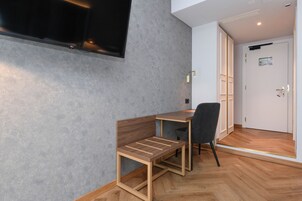 Una camera moderna con una scrivania in legno, una sedia, una TV a schermo piatto montata al muro e una porta con un cartello.