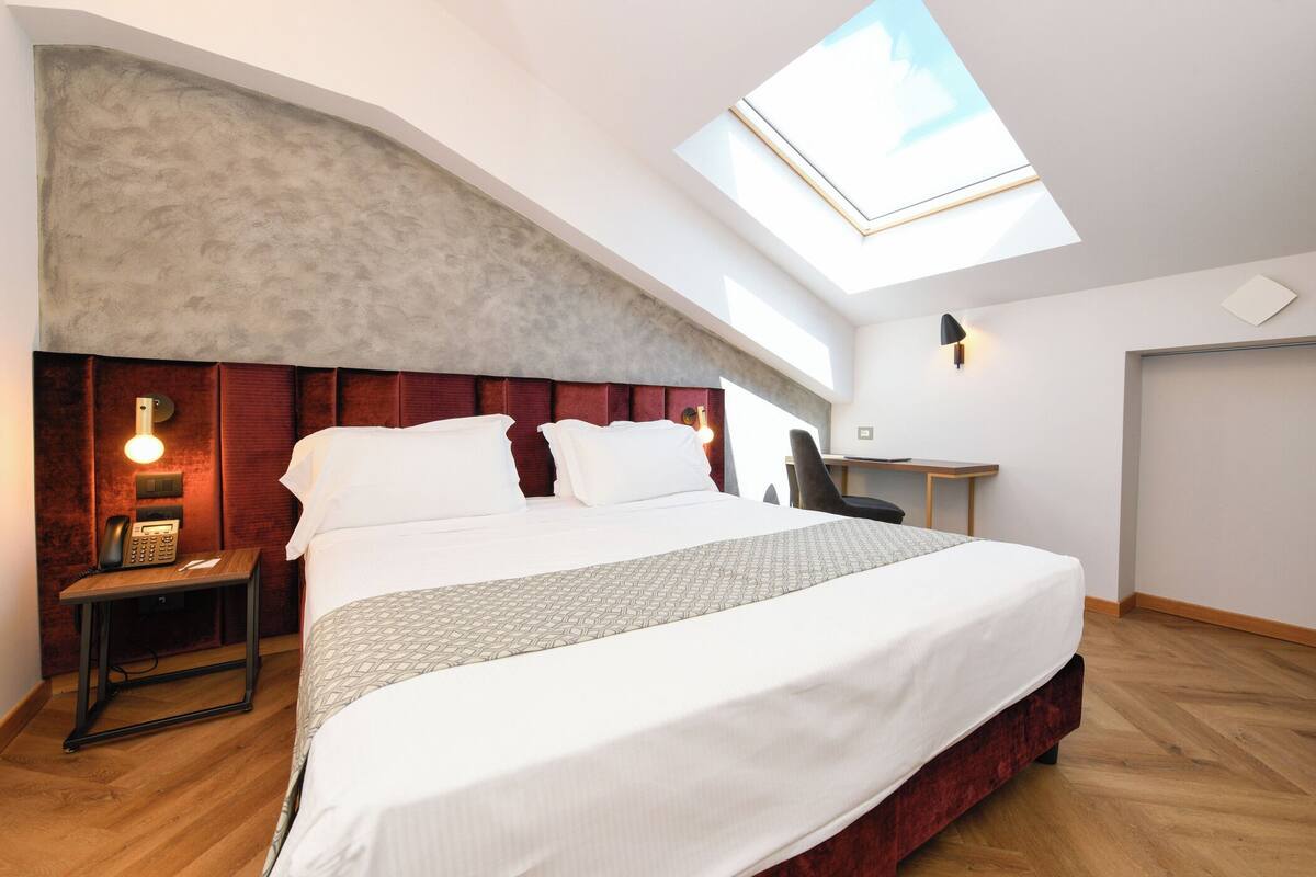 A modern hotel room with a skylight, a large bed, a desk, and a telephone on a nightstand.
