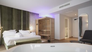 A modern hotel room with a large bed, a glass-enclosed walk-in closet, a sitting area with a chair, and a large bathtub. - Palazzo Santo Spirito (Bergamo)