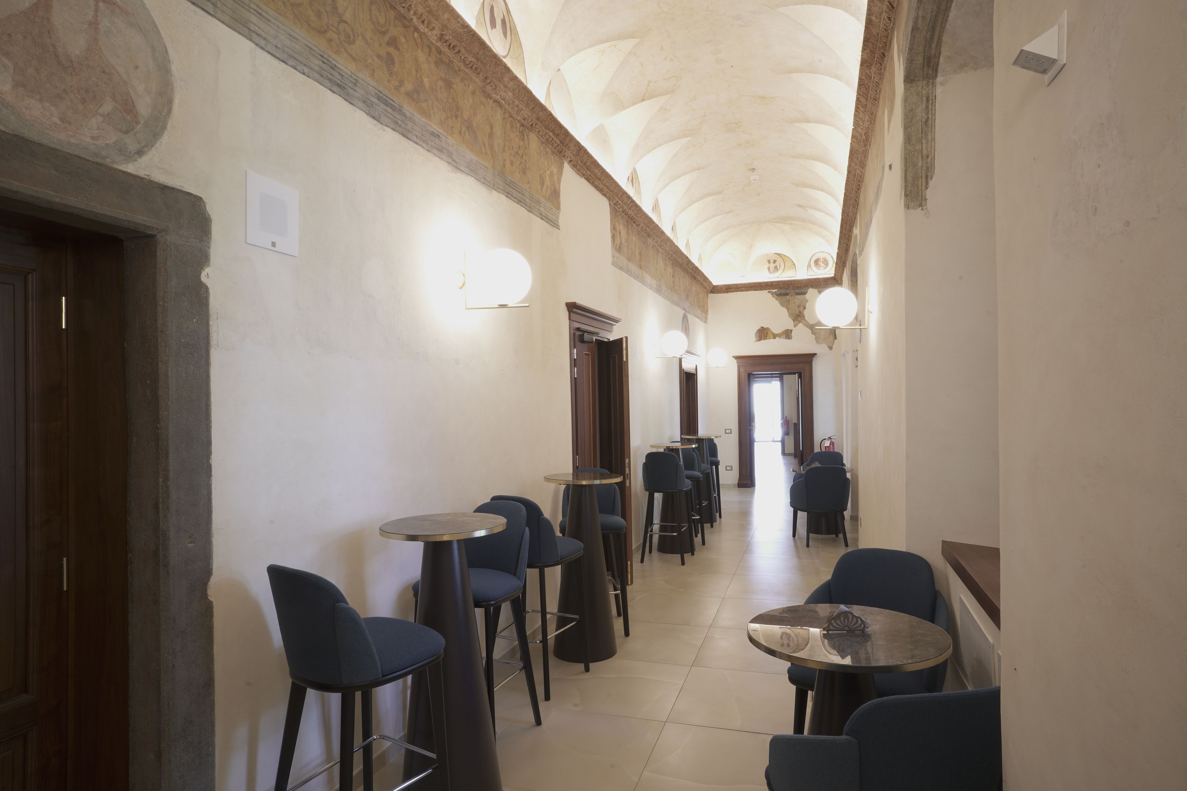 A corridor with bar stools and tables, a wooden door, and a ceiling with decorative elements.