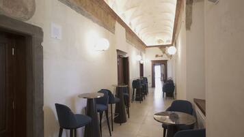A corridor with bar stools and tables, a wooden door, and a ceiling with decorative elements.