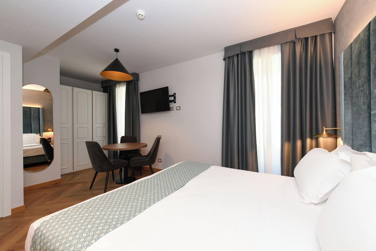A hotel room with a bed, a desk, chairs, a television, and a window with curtains.