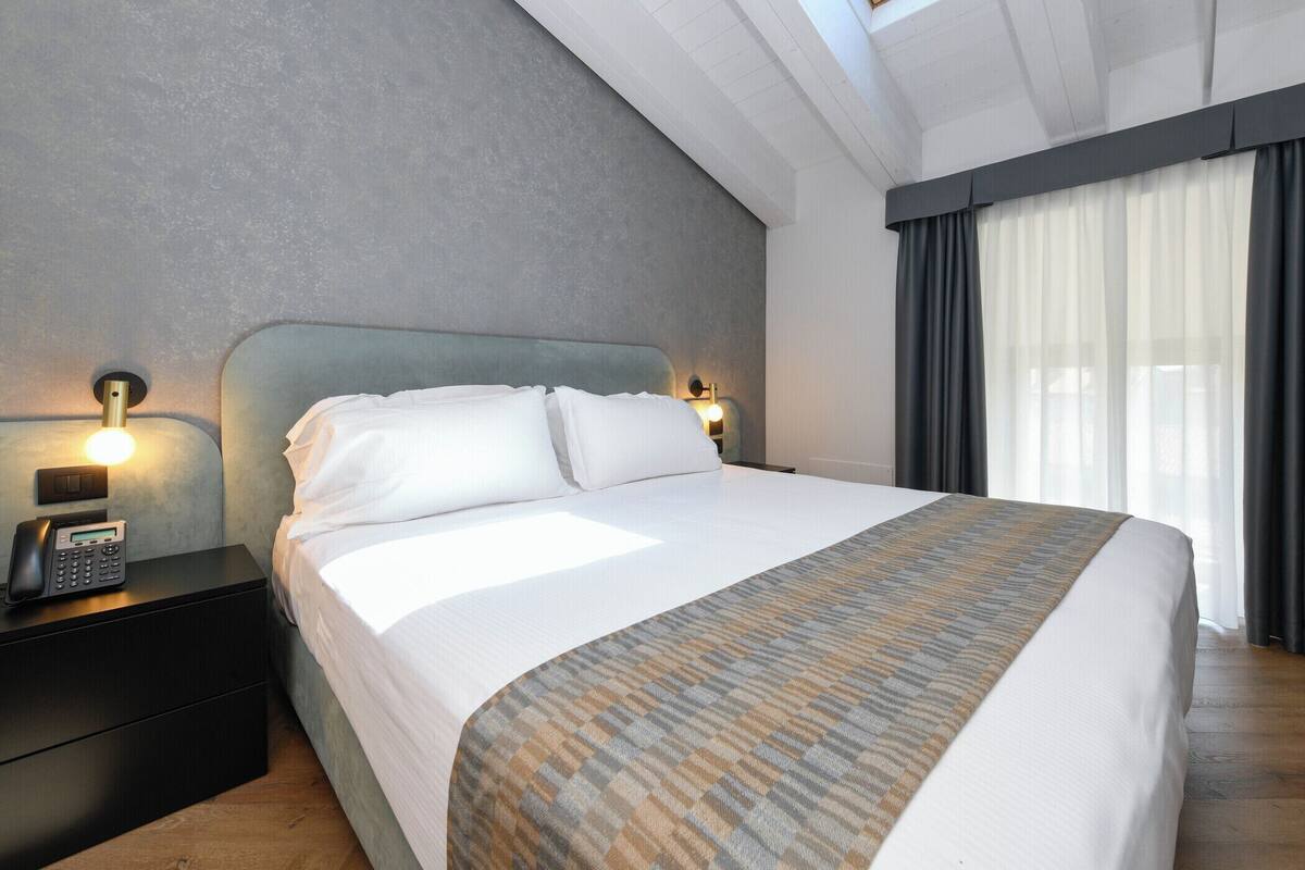 A modern hotel room with a large bed, a bedside phone, and a nightstand.