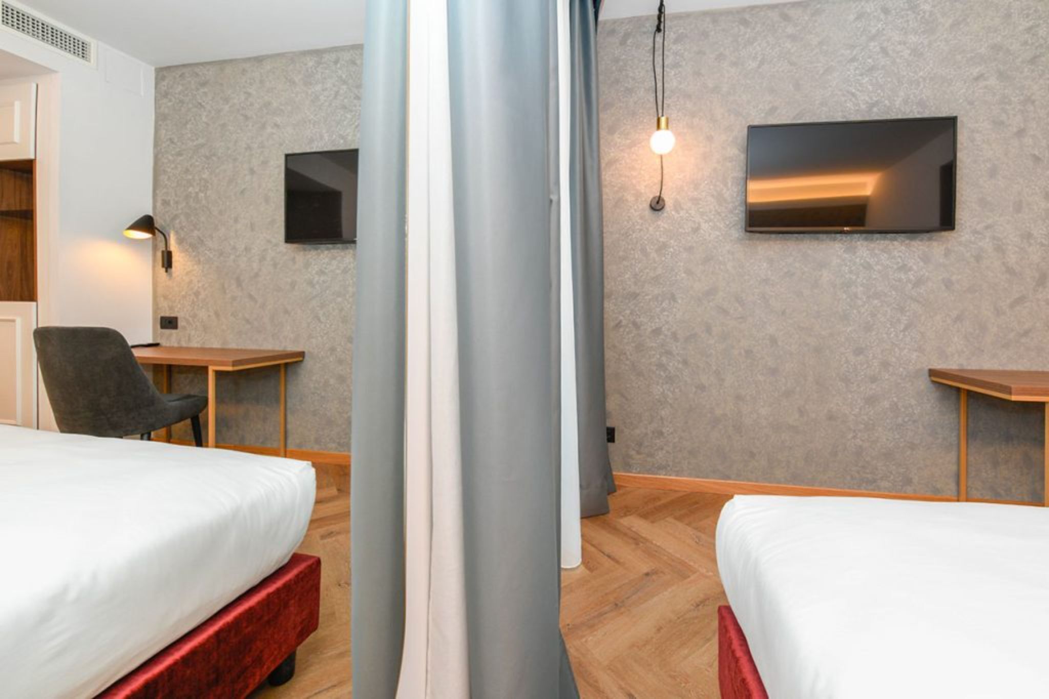 Una camera d'albergo con due letti, una scrivania, una sedia e un televisore montato a parete.