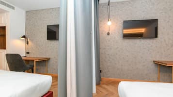 Una camera d'albergo con due letti, una scrivania, una sedia e un televisore montato a parete.