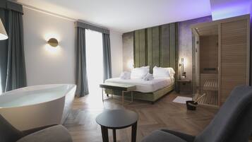 A modern hotel room with a large bed, a bathtub, a seating area, and a walk-in closet.