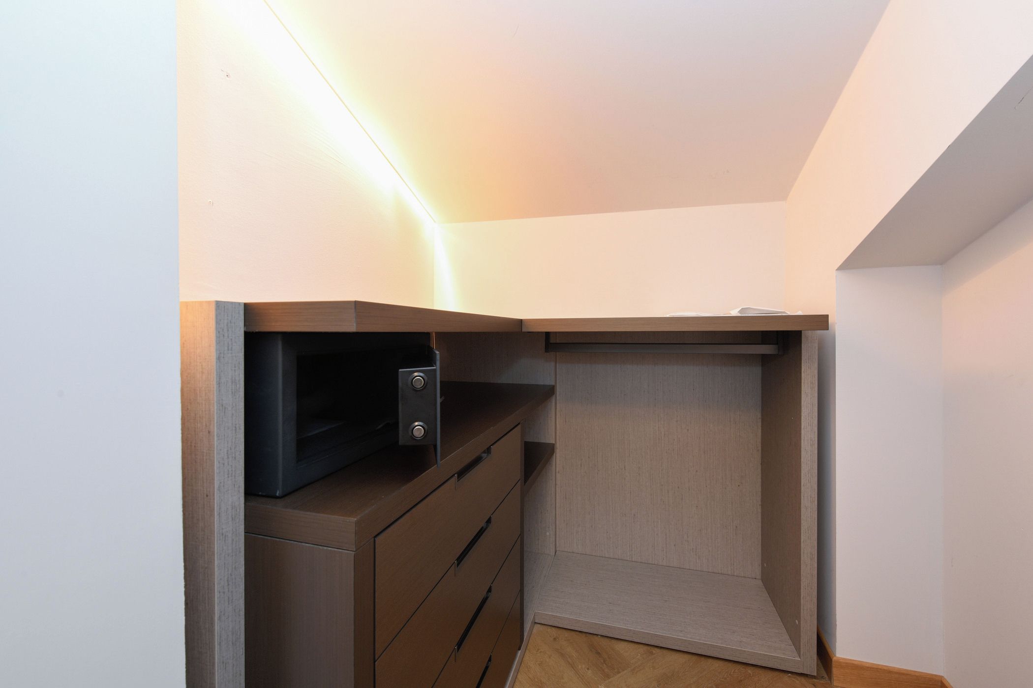 Quarto compacto com roupeiro embutido, micro-ondas e um pequeno espaço para prateleiras.