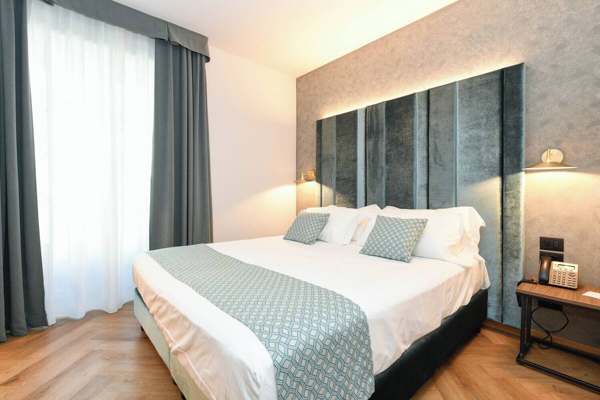 A modern hotel room with a large bed, a bedside telephone, and a nightstand.