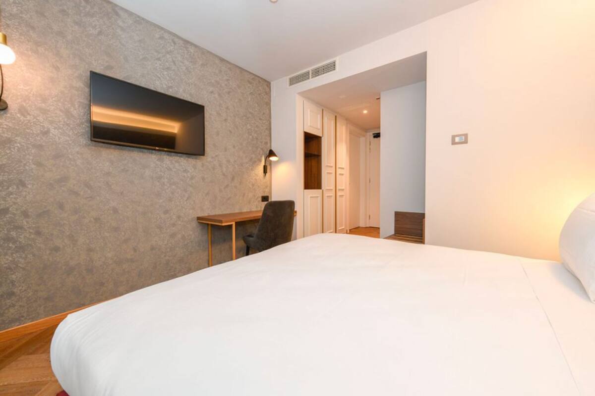 A hotel room with a large bed, a desk, a chair, and a wardrobe.