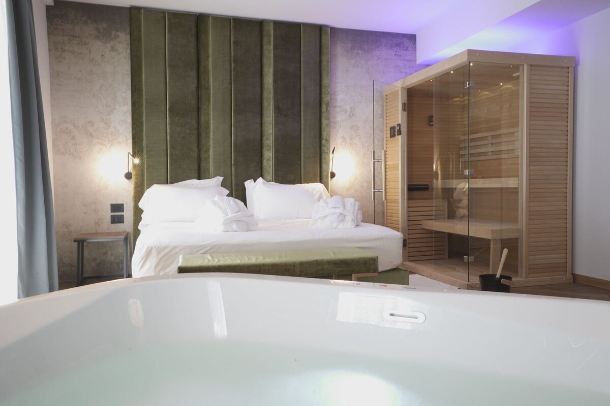 A modern hotel room with a large bed, a glass-enclosed wardrobe, and a small bedside table.