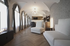 A modern hotel room with a wooden floor, a sofa, a chair, a TV, and a small table. - Palazzo Santo Spirito (Bergamo)