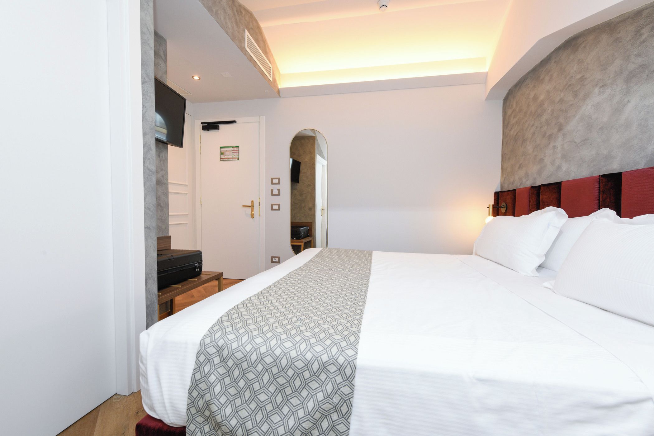 Ein Hotelzimmer mit einem großen Bett, einer hölzernen Bank, einem Fernseher und einer Tür zu einer Treppe.
