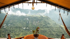 A wooden deck with a round table and two chairs, overlooking a mountainous landscape. - El Nido del Cóndor Ecolodge (Villamaria)