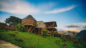 A unique wooden structure with multiple levels and a sloped roof, surrounded by lush greenery and a clear sky. - El Nido del Cóndor Ecolodge (Villamaria)