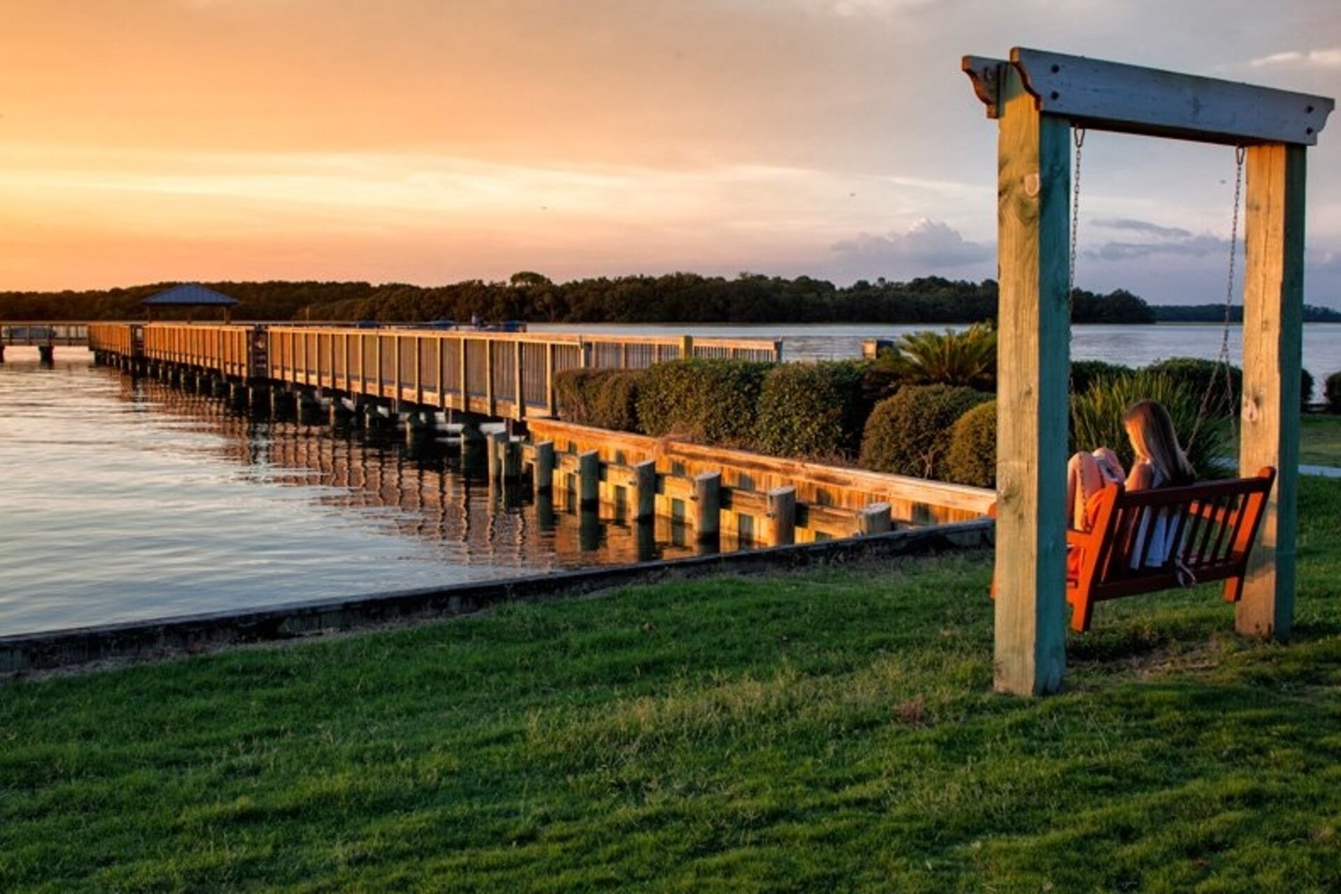 Une jetée en bois s’étendant sur une étendue d’eau calme, avec un banc et une personne assise dessus.