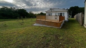 Ein eingeschossiges Haus mit einer Holzterrasse, umgeben von einem Rasen und einem Holzzaun.