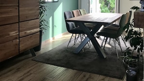 A dining area with a wooden table and chairs, a mirror on the wall, and a view of greenery outside. - Quiet house with enclosed garden and terrace 5 minutes from the beach! (Travo)