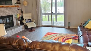 Een woonkamer met een open haard, een leren bank en een groot raam met uitzicht op een groen landschap.