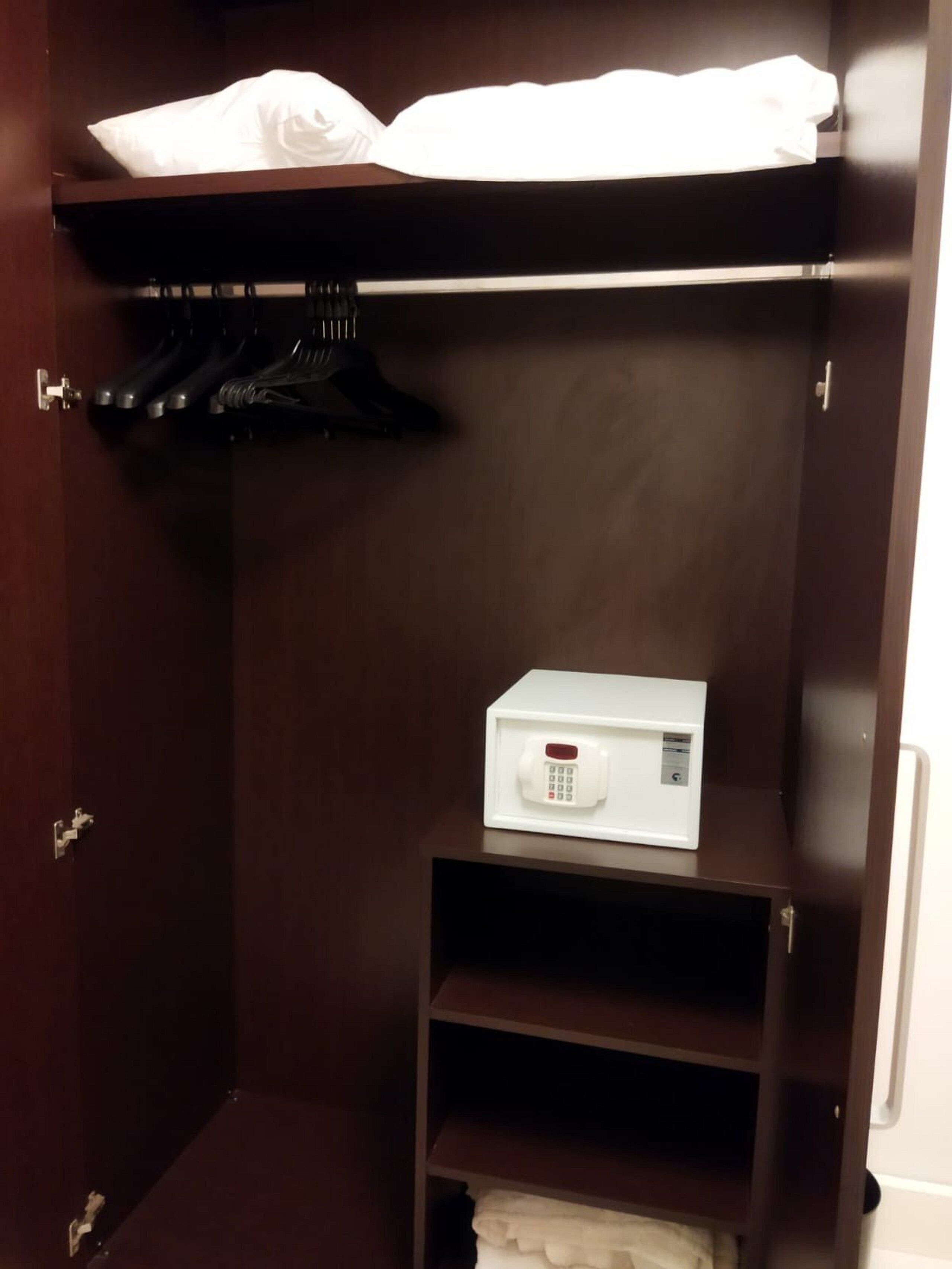 A dark wooden wardrobe with a white box on the lower shelf, a hanging area above, and a door with a handle.