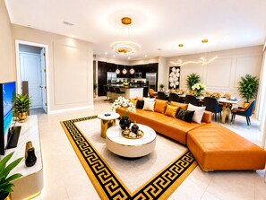 Ein modernes Wohnzimmer mit einer Eckcouch, einem runden Couchtisch und einem Essbereich mit einer großen Blumenkomposition.