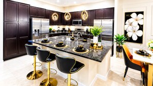 A modern kitchen with dark wood cabinets, stainless steel appliances, a marble island, and gold accents.