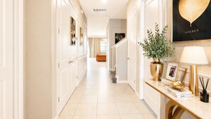A hallway with white doors, a plant, a framed picture, and a lamp on a console table.
