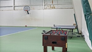 Een binnensportgelegenheid met een tafelvoetbaltafel, een pingpongtafel en een basketbalring.
