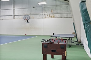 Un centre sportif intérieur équipé d’une table de baby-foot, d’une table de ping-pong et d’un panier de basket.