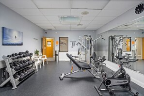 Un gimnasio con equipamiento de ejercicio, una banca y un estante con mancuernas.