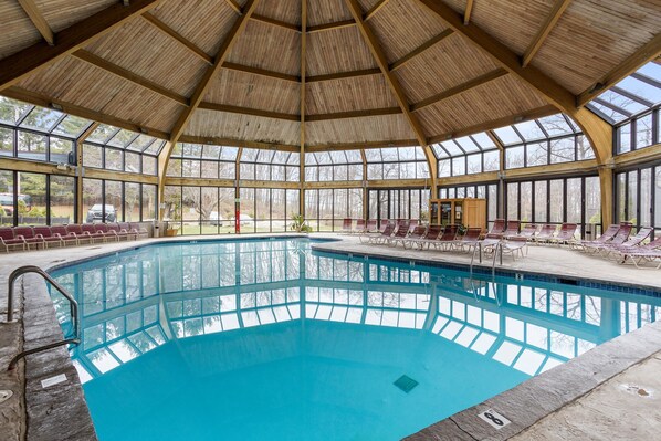 Un'ampia piscina interna con tetto in legno e pareti in vetro, circondata da sdraio.