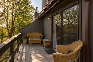 A balcony with wicker furniture, a potted plant, and a view of trees.