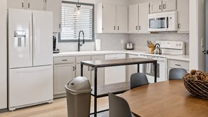 Een moderne keuken met witte kasten, een roestvrijstalen spoelbak, een magnetron en een eethoek met tafel en stoelen.