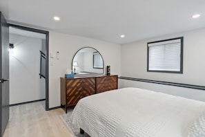 A bedroom with a bed, a dresser, a mirror, and a window with blinds.