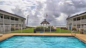 Ein Schwimmbecken mit einem Pavillon im Hintergrund, umgeben von einem weißen Zaun und zwei Gebäuden.