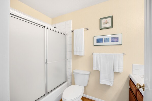 A bathroom with a shower, toilet, and two framed pictures on the wall.