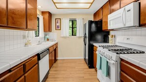 A kitchen with wooden cabinets, a white countertop, a black refrigerator, a white stove, and a microwave. - Cozy place in quaint, fun city (Sierra Madre)