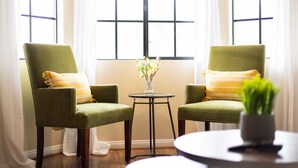 Two green armchairs with yellow pillows, a small table with a vase of flowers, and a round table with a plant. - Cozy place in quaint, fun city (Sierra Madre)