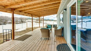 Eine Holzterrasse mit Gartenmöbeln und einer Glastür zu einem überdachten Bereich.