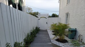 A narrow wooden pathway flanked by white fences and plants, leading to a white building with a door and windows. - Historic Intimate Studio A (Haines City)