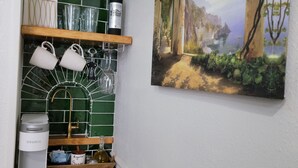 A kitchen with a green tiled backsplash, a coffee maker, and a wine bottle on the counter. - Historic Intimate Studio A (Haines City)