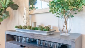 Una consola de madera con un florero de vidrio y adornos esféricos, rodeada de copas de cristal.