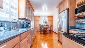 Una cocina con armarios de madera, electrodomésticos de acero inoxidable, encimera de granito y un comedor con candelabro.