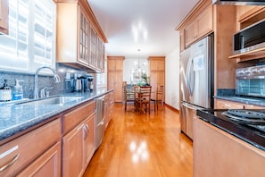 A kitchen with wooden cabinets, stainless steel appliances, a granite countertop, and a dining area with a chandelier. - Spacious 4BR Home w/ Stunning Views Near SF (South San Francisco)