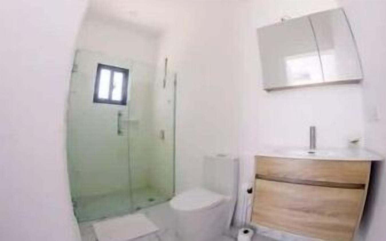 A small bathroom with a toilet, a glass shower enclosure, and a wooden vanity with a mirror.
