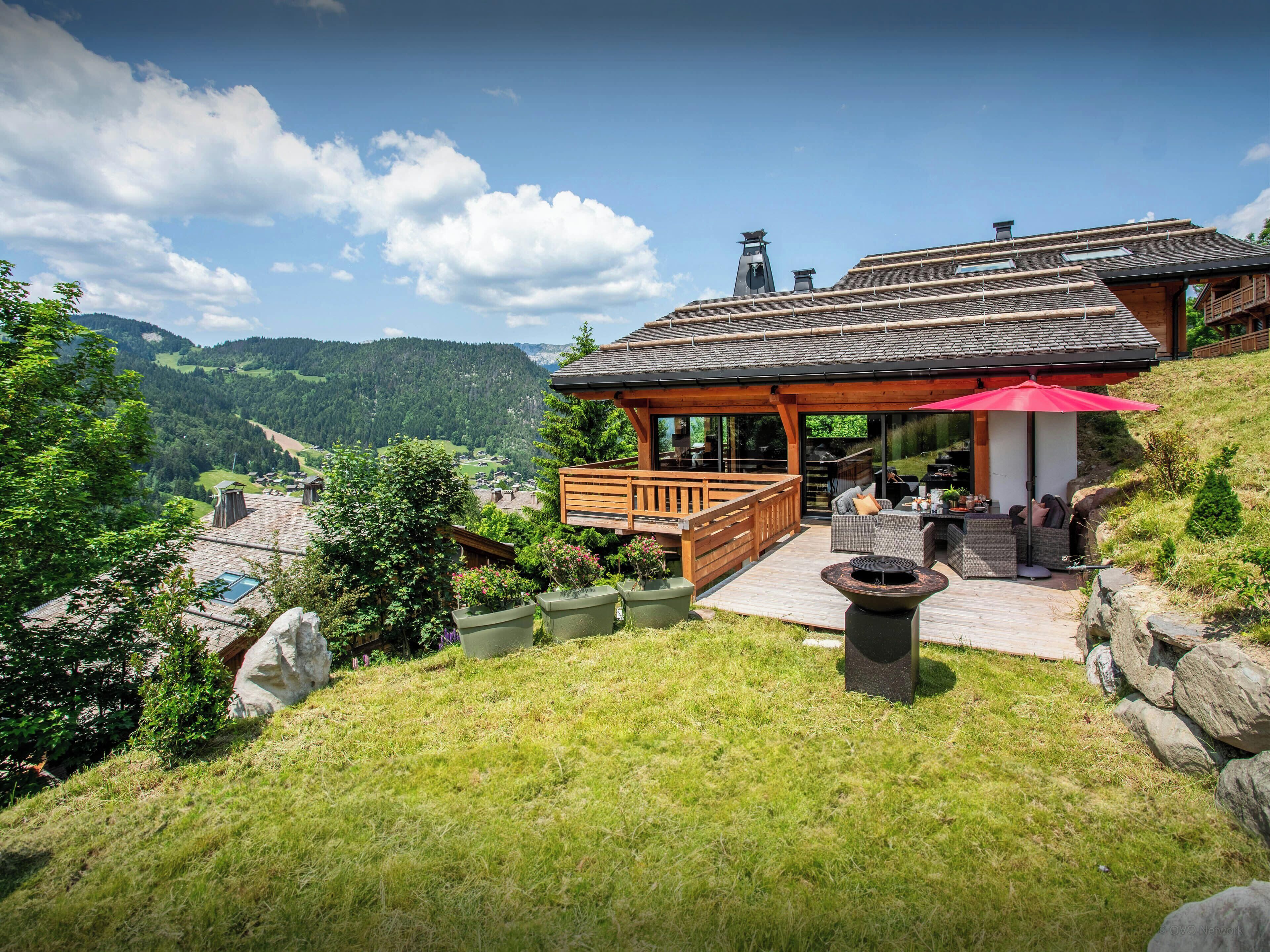 Un chalet doté d’une terrasse en bois, d’un espace salon extérieur et offrant une vue sur les montagnes environnantes.