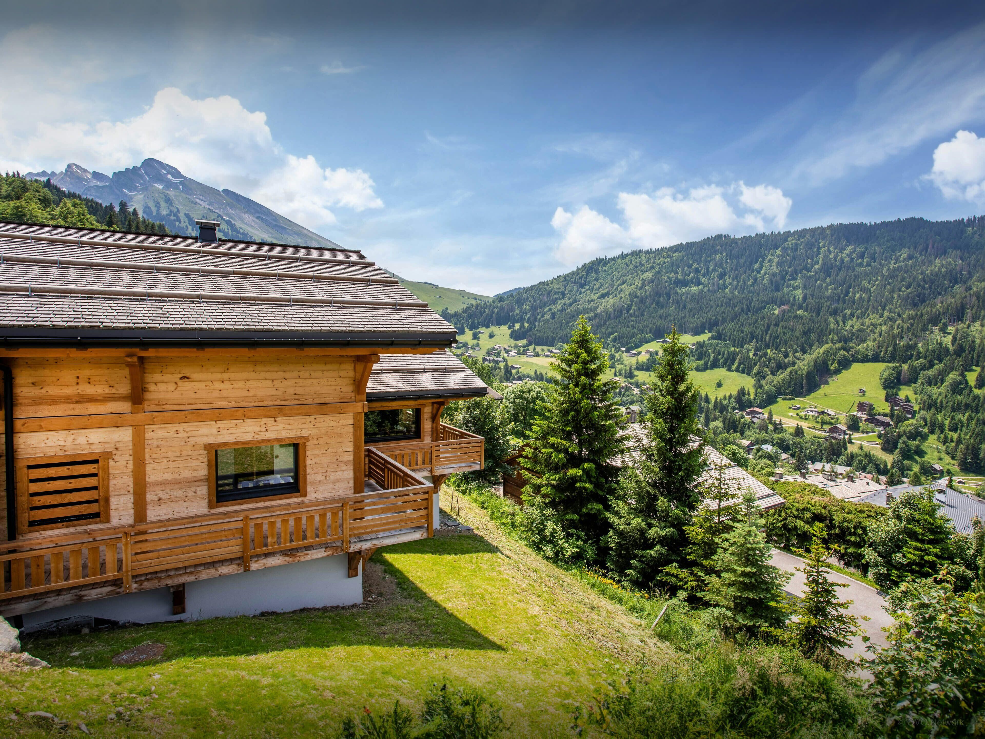 Un chalet en bois doté d’un balcon donnant sur une vallée et des montagnes.