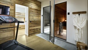 Een moderne hotelkamer met een houten wand, een loopband, een glazen douchecabine en een badjas hangend aan een rek.