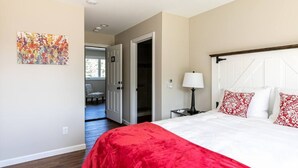 Une chambre avec un grand lit, une porte donnant sur un couloir et une petite table avec une lampe.