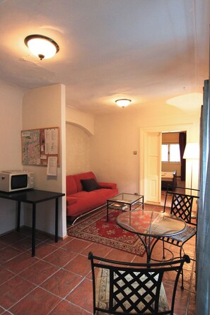 Un espacio habitable compacto con kitchenette, un sofá rojo, una mesa de vidrio y un tapete estampado.